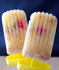 two popsicles sitting next to each other on top of a yellow container filled with fruit