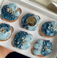 four cupcakes with blue frosting and pearls on them in a white box