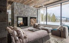 a bedroom with a stone fireplace and large windows overlooking the snow covered mountain side area