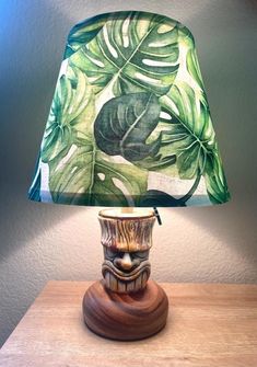 a lamp that is sitting on top of a wooden table with a green leaf print shade