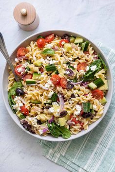 a bowl filled with pasta salad next to a wooden spoon