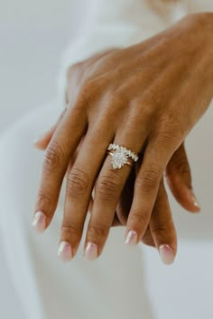 a close up of a person's hand with a ring on their finger, wearing a white dress