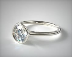 a white gold engagement ring with an oval cut diamond in the center, on a plain surface