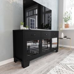 a large mirror on top of a black cabinet next to a rug and table in front of a window