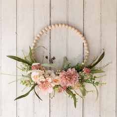 a wreath with pink flowers and greenery hangs on a white wooden wall in front of a door