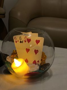 a lit candle sits in front of a glass bowl filled with playing cards