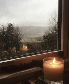 a candle sitting in front of a window on a rainy day