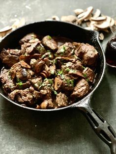 a skillet filled with meat and mushrooms next to a bottle of wine on a table