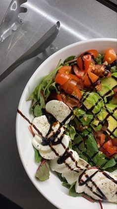 a salad with mozzarella, tomatoes and avocado in a white bowl