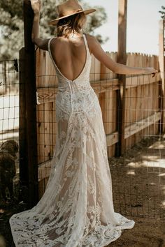 a woman in a white dress and hat leaning against a fence with her back to the camera