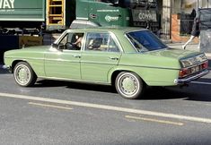 an old green car parked on the side of the road in front of a truck