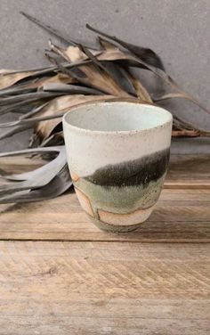 a cup sitting on top of a wooden table next to dry grass and dried plants