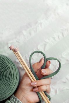 a woman holding two knitting needles next to a ball of yarn