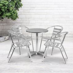 three chairs and a table in front of a brick wall with a potted tree