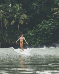 a woman riding a wave on top of a surfboard in the ocean next to palm trees