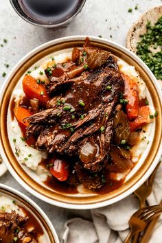 a bowl filled with meat and vegetables on top of mashed potatoes next to a glass of wine