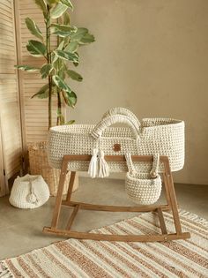 a white wicker baby's cradle sitting on top of a rug next to a potted plant