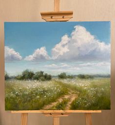 an easel holding up a painting of a dirt road in the middle of a field