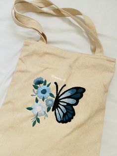 an embroidered butterfly and flowers on a tote bag sitting on top of a bed