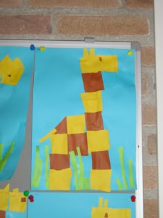 a paper giraffe made to look like it is standing in the grass next to a brick wall