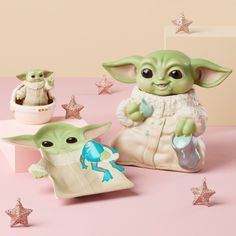 two baby yoda toys are sitting next to each other on a pink surface with stars around them