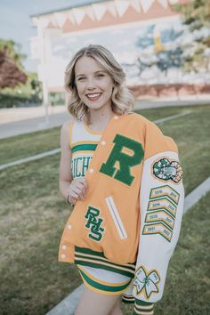 A cheerleader shows off her patches on her Varsity letterman jacket. She is on the richland high school campus. Varsity Jacket Cheerleader, Soccer Letterman Jacket Ideas, Letterman Photoshoot, Senior Picture Ideas Letterman Jackets