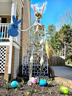 a skeleton with bunny ears standing in front of a house next to easter eggs on the ground