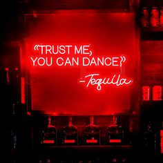 a red neon sign that says trust me you can dance tequila in front of liquor bottles