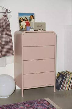 a pink dresser sitting next to a wall with pictures on it and a rug in front of it