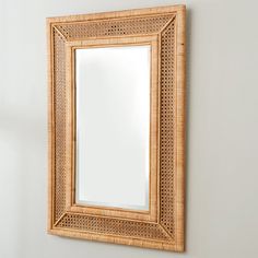 a mirror hanging on the wall next to a white wall with a rattan frame