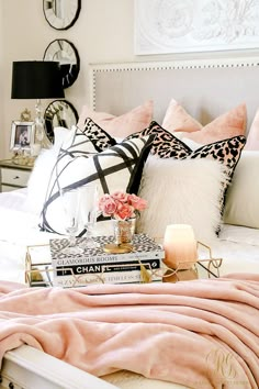 a white bed topped with lots of pillows next to a pink blanket and two candles