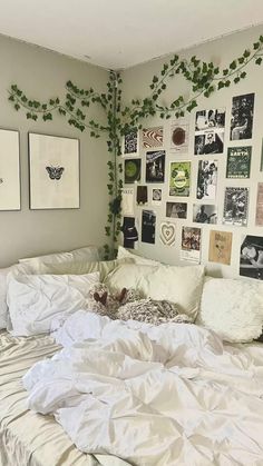 an unmade bed with many pictures on the wall and plants growing up above it