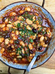 a large bowl filled with lots of food on top of a wooden table next to a spoon