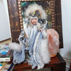 there is a small doll sitting on a table next to some books and a painting