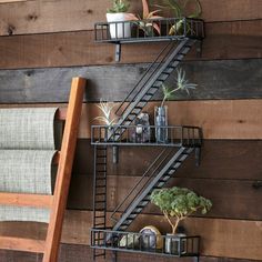 a set of metal shelves with plants on them against a wooden wall next to a ladder