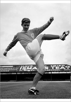 a man kicking a soccer ball on top of a grass covered field in front of a stadium