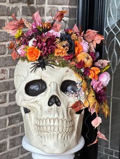 a white skull with flowers in it's head sitting on a pedestal next to a brick wall