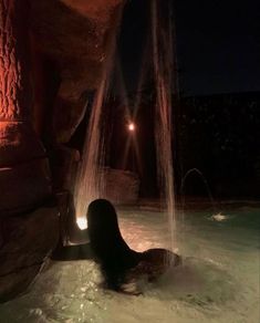 a woman is in the water at night with her back turned to the camera and lights on