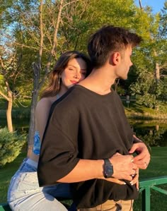 a man and woman standing next to each other in front of a lake with trees