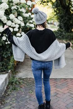 a woman is walking down the sidewalk with her hands in her pockets and wearing a gray knitted pom - pom hat