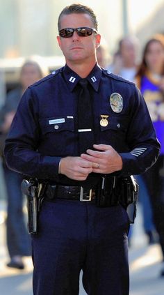 a police officer standing on the street with his hands in his pockets and people behind him