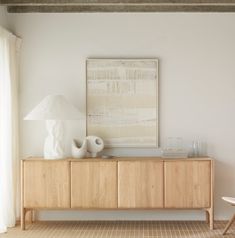 a white vase sitting on top of a wooden cabinet next to a lamp and window