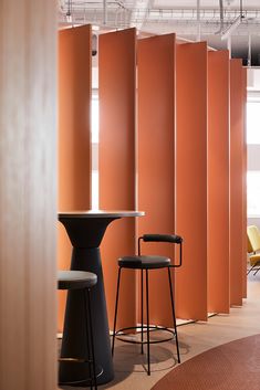 two stools and a table in an office setting with orange partitions behind them