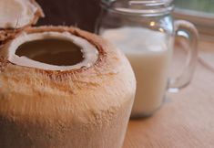 two coconuts sitting on top of a wooden table next to a glass of milk