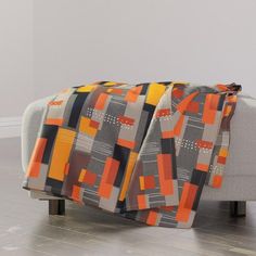 an orange and grey blanket sitting on top of a white couch next to a wooden floor