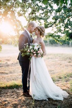 a bride and groom standing under a tree