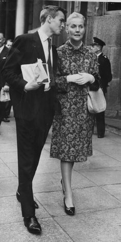 an old black and white photo of a man and woman walking down the street together