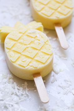 two pops with pineapple slices on them sitting on some white lace and one has a wooden stick sticking out of it