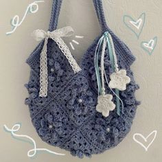 a crocheted purse hanging on a wall with hearts and ribbons attached to it