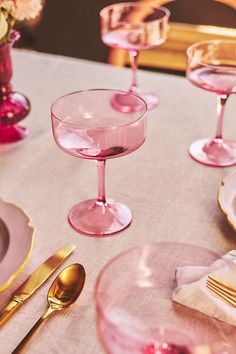 the table is set with pink wine glasses and gold cutlery, along with silverware